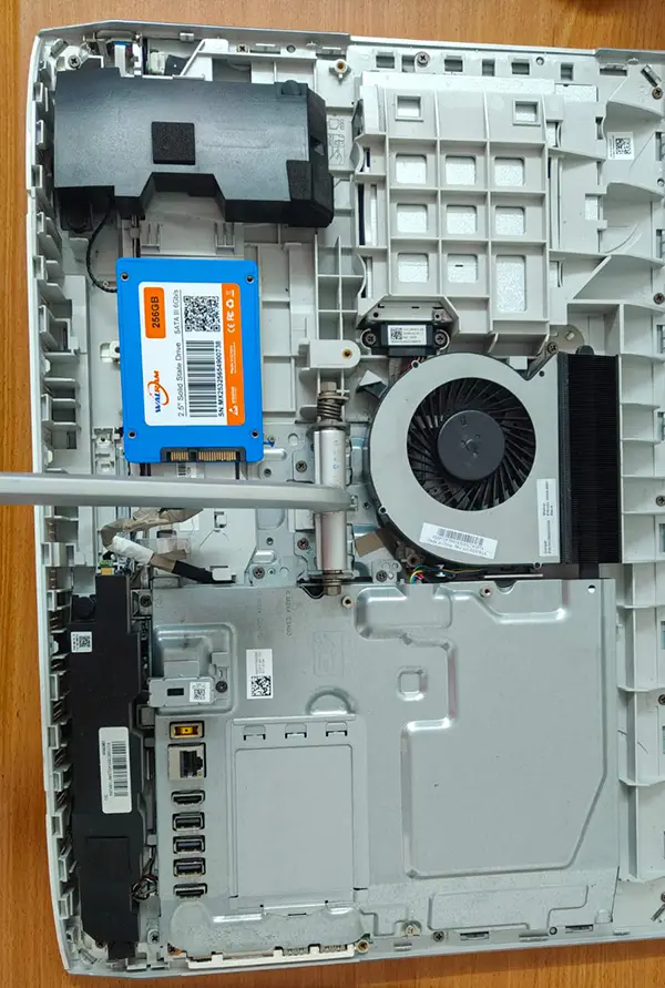 Primer plano del interior desarmado de un computador de escritorio Lenovo Todo en Uno (All-in-One) sobre la mesa de trabajo del servicio técnico de Tecnocom Valle. Se observa el componente causante de la lentitud: un disco duro mecánico original marca WD Blue de 1.0TB de 3.5 pulgadas, ubicado junto al ventilador de refrigeración tipo turbina y el blindaje metálico de la placa base. En la imagen también destaca un destornillador de precisión eléctrico, ilustrando el delicado proceso de mantenimiento y desarme preventivo para clientes en Cali, Buga, Tulúa y el Valle del Cauca.